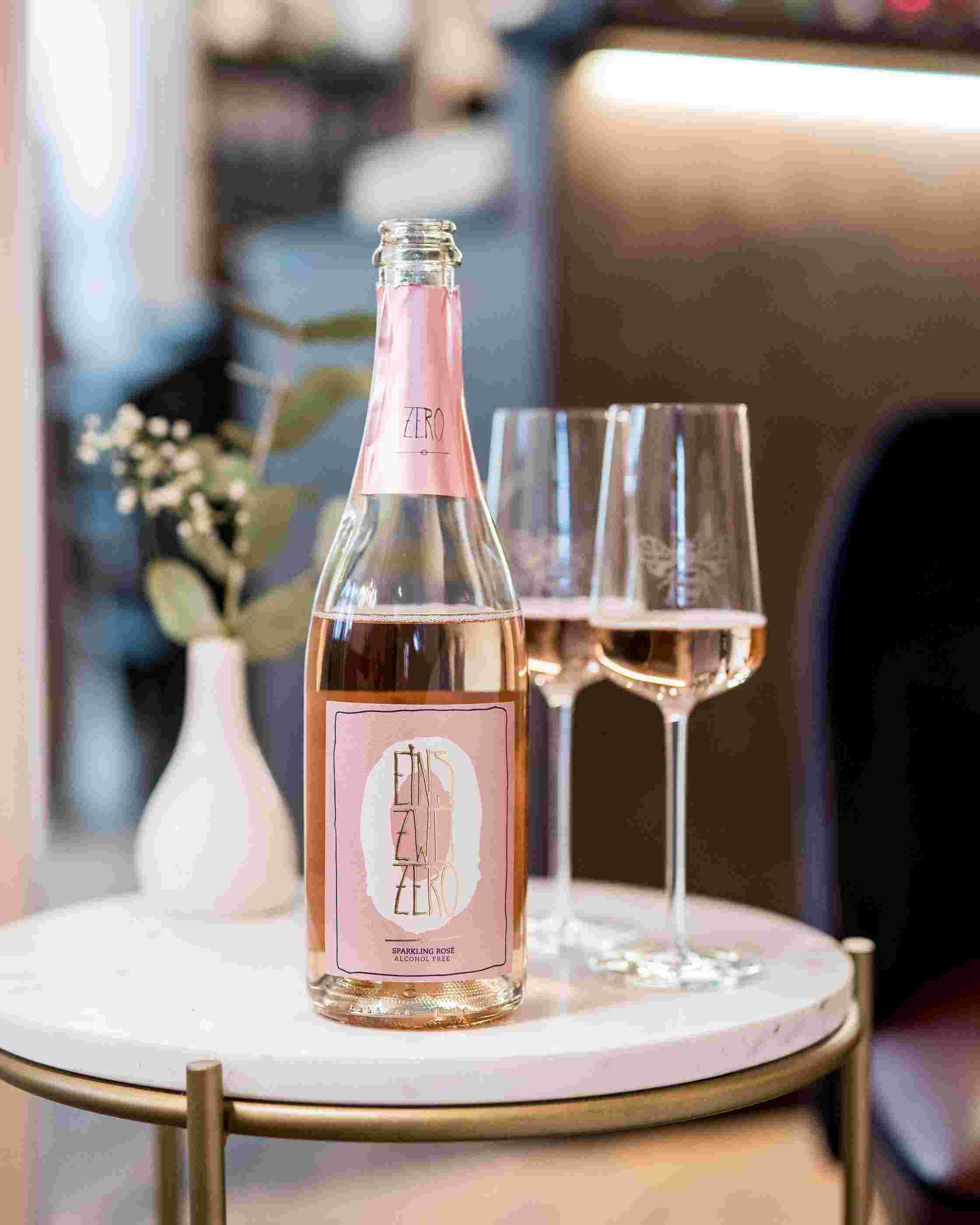 Sfeerfoto Leitz Eins-Zwei-Zero Riesling Sparkling Rosé. Op de achtergrond staan twee halfgevulde wijnglazen.