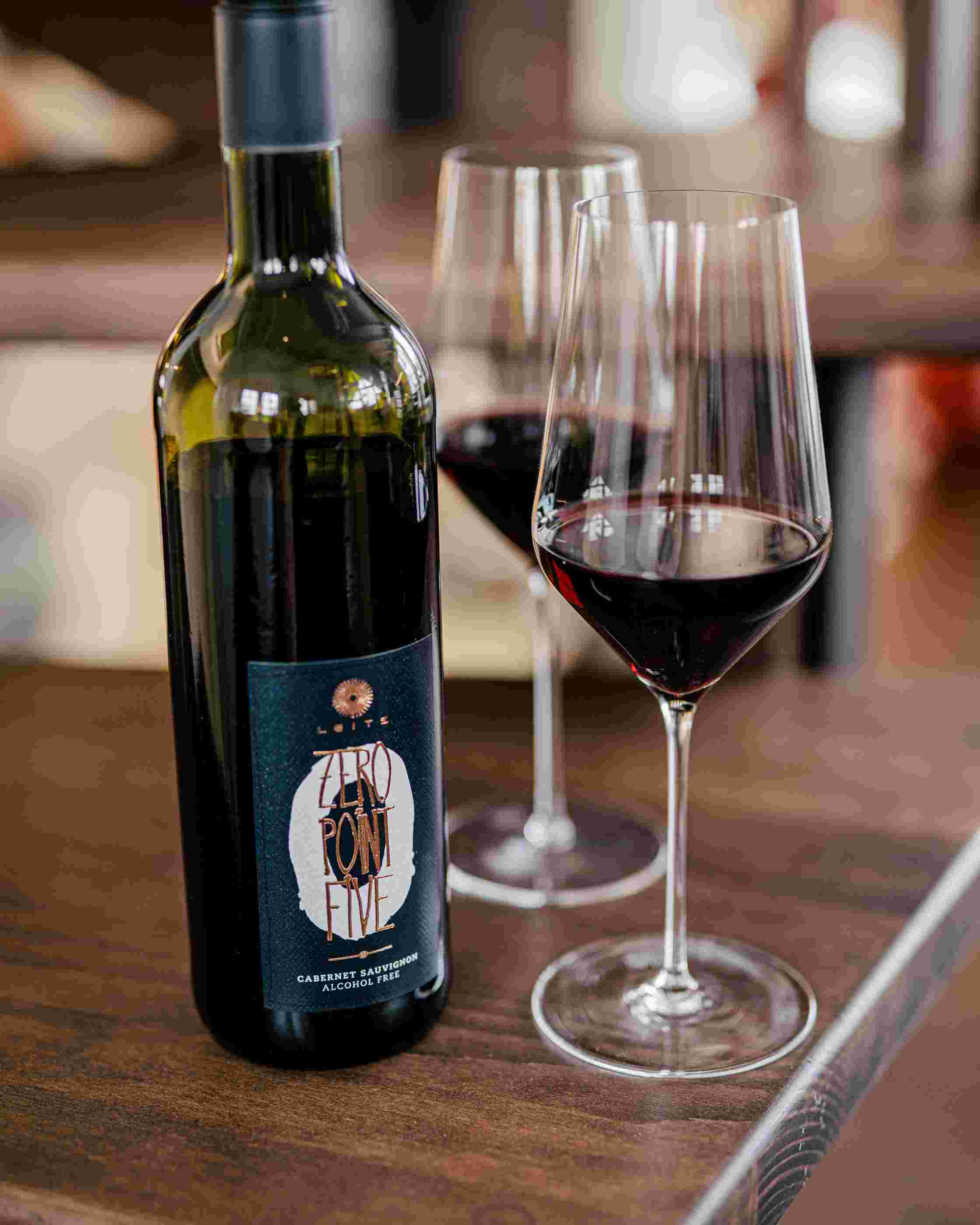 Sfeerfoto Leitz Zero-Point-Five Cabernet Sauvignon. De fles staat op een donkere houten tafel, naast twee wijnglazen.