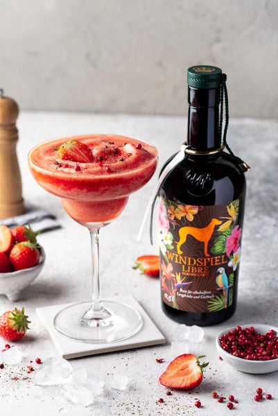 Sfeerfoto van een fles Windspiel Libre Alcoholvrije Rum. Op de foto staat links een glas met daarin een Aardbeien Daquiry, gemaakt van de Windspiel Libre Alcoholvrije Rum.