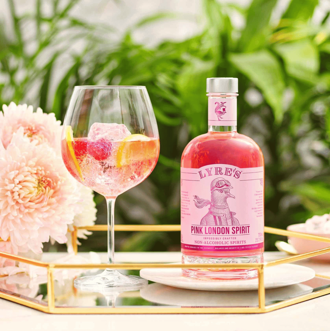 Sfeerfoto van Lyre's  Pink London Spirit - Alcoholvrije gin. Rechts staat de fles Lyre's  Pink London Spirit - Alcoholvrije gin, links staat een mooi cocktailglas met daarin een drankje. 